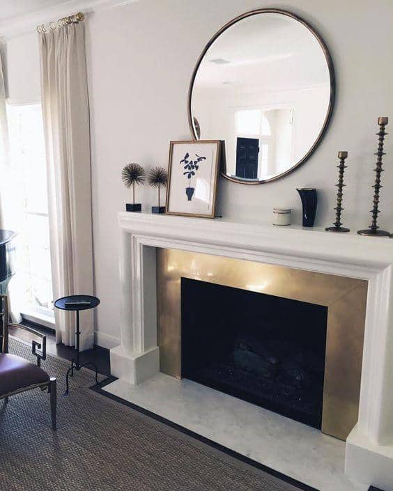 Modern fireplace mantel with round mirror, gold accents, and minimal decorative pieces.