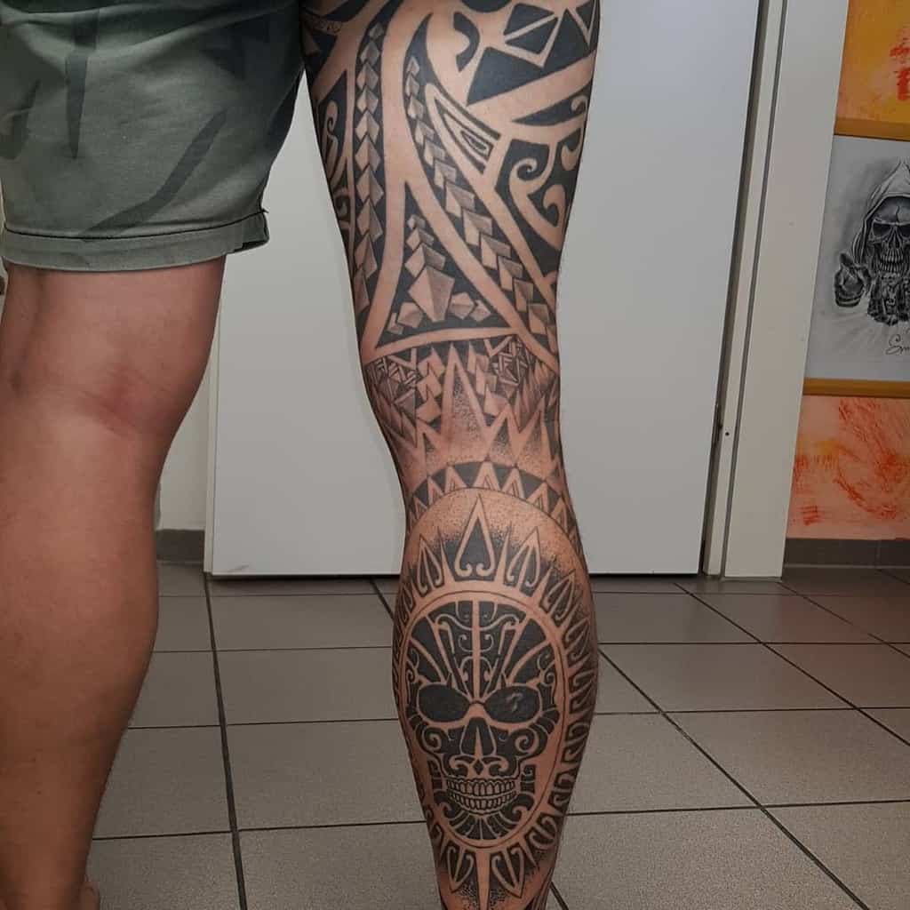 Tribal leg sleeve tattoo featuring bold geometric patterns, with a prominent skull design and intricate details