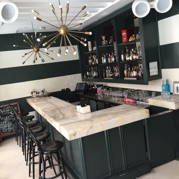 Polished marble bar top with black stools and gold starburst chandeliers in a chic, modern bar setup.