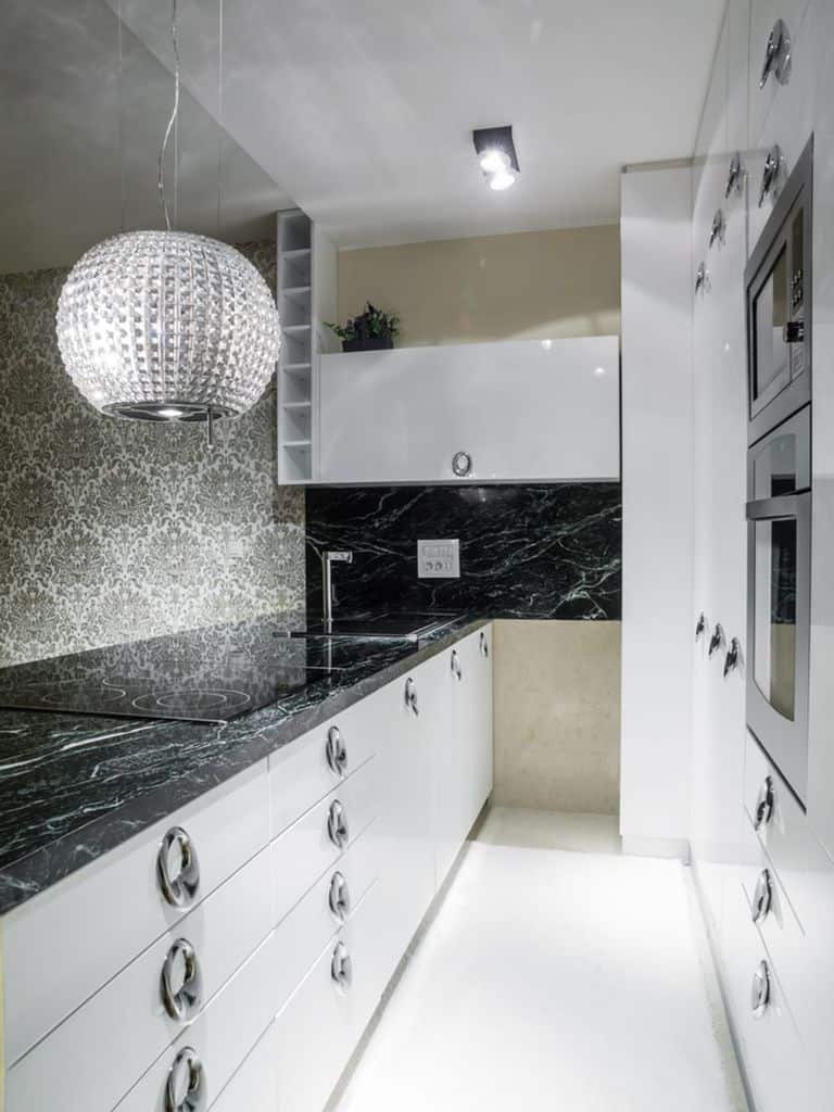 Modern kitchen with black marble countertops, white cabinets, and a crystal pendant light.