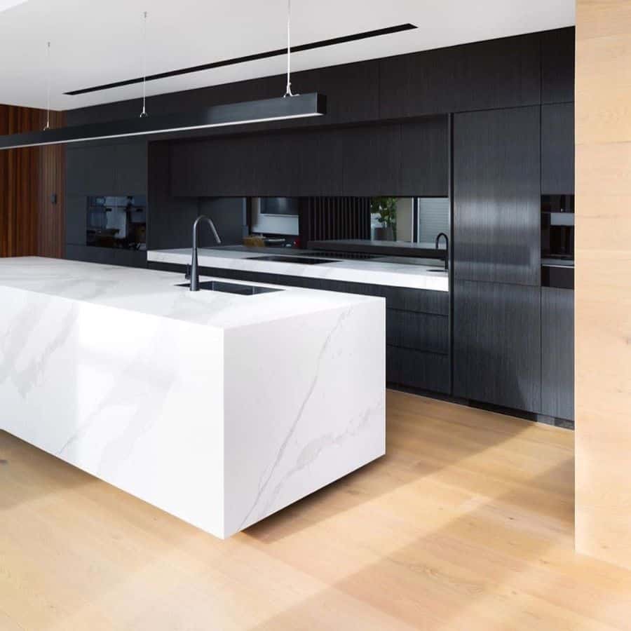 Modern kitchen with black cabinets, white marble island, and light wood flooring.