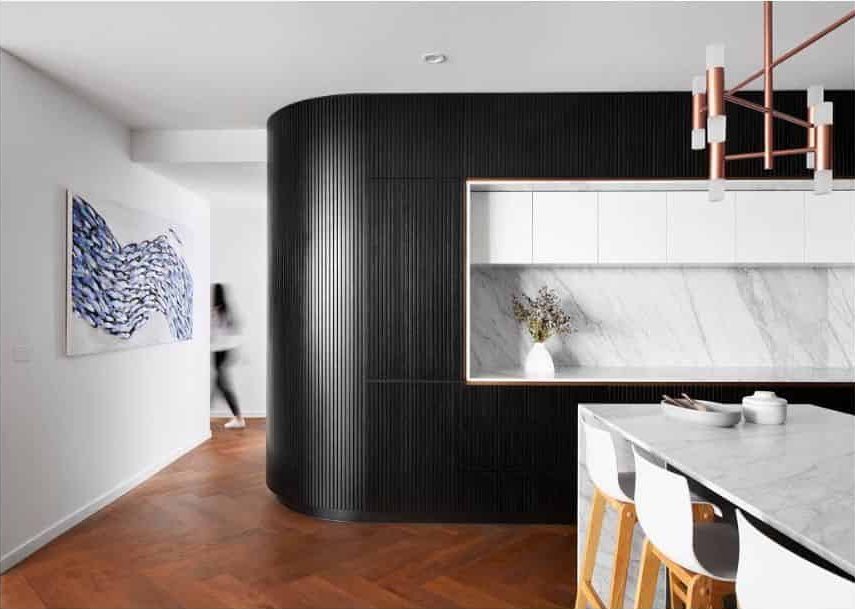 Modern kitchen with black paneled walls, white marble countertops, and copper chandelier.