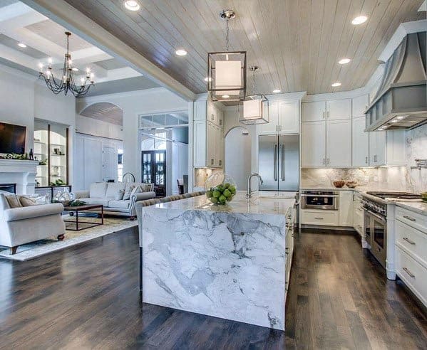 White kitchen with marble waterfall island, wood ceiling, and dark hardwood flooring.