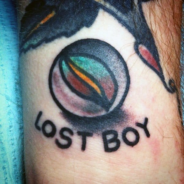 Tattoo of a detailed marble with the words "Lost Boy" underneath, symbolizing nostalgia and childhood with bold shading and vibrant colors.