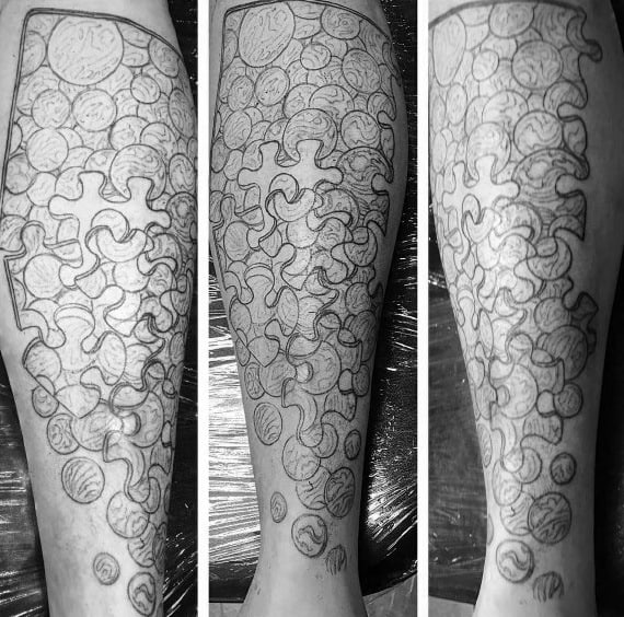 Black and gray leg tattoo featuring marbles and puzzle pieces blending together, creating a unique and intricate design with deep symbolism.