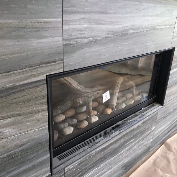 Gas fireplace with a black frame set in a gray marble tile surround and stone accents inside.