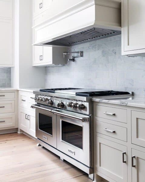 Bright kitchen with white cabinetry, a light marble tile backsplash, stainless steel range, and sleek modern hardware