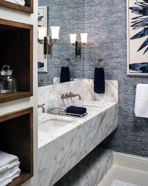 Luxury bathroom with marble vanity, textured blue walls, and wall sconces.