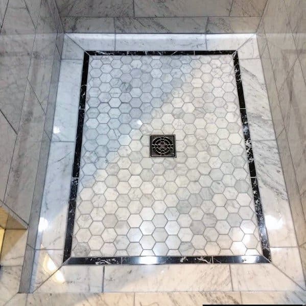 Hexagonal tiles and a central drain grace the shower floor, edged in black marble trim