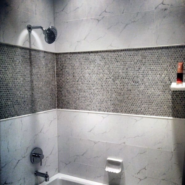 Modern shower with marble tiles, a gray mosaic accent strip, showerhead, and small wall shelf