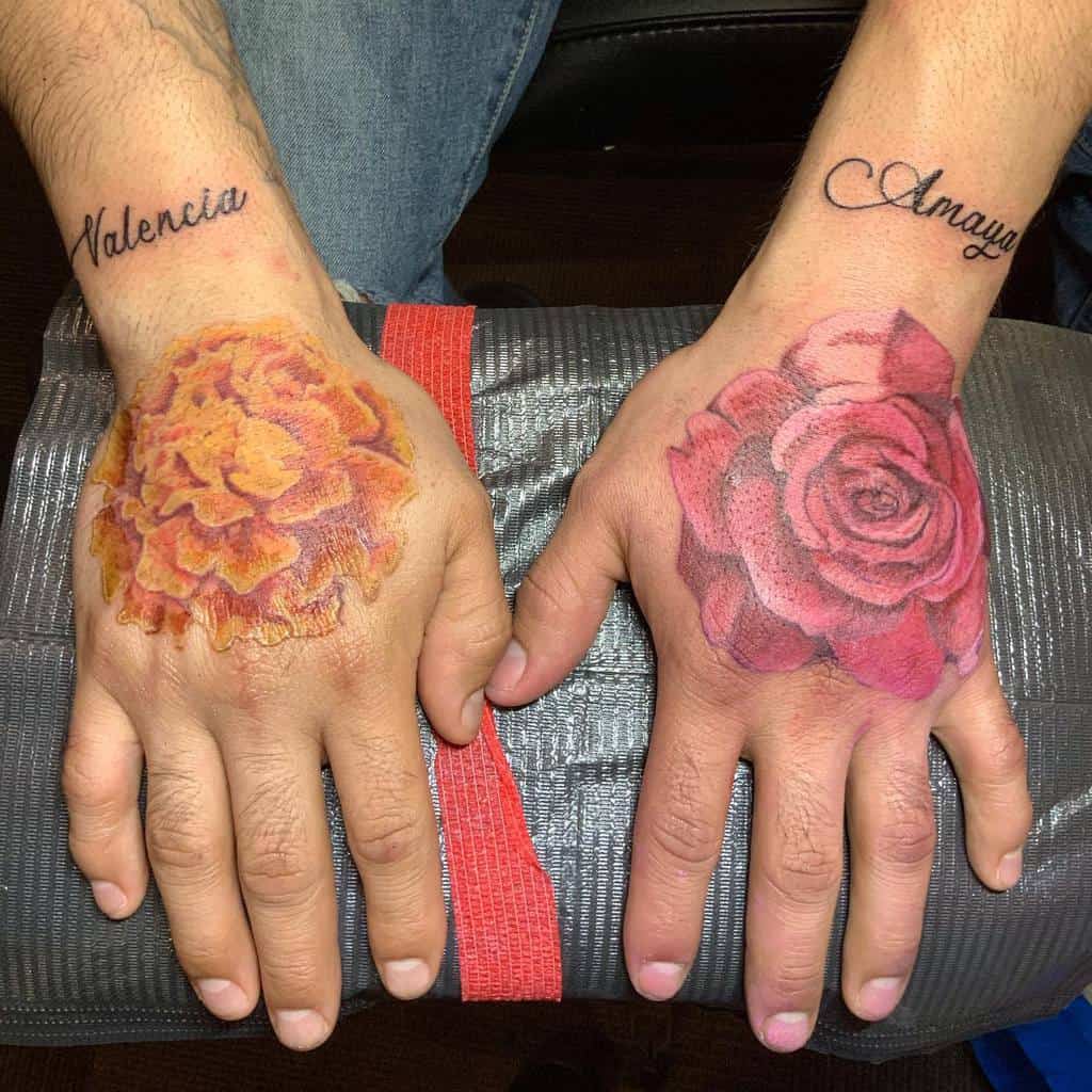 Tattoos featuring a vibrant orange marigold on one hand and a detailed red rose on the other, with cursive script names "Valencia", and "Amaya"