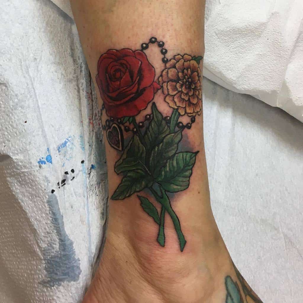 A red rose and a yellow marigold with green leaves, connected by a beaded chain with a heart pendant