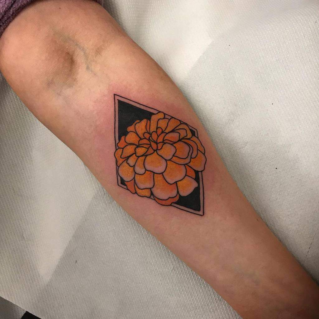 Bold geometric tattoo featuring an orange marigold inside a black diamond frame, creating a striking contrast with clean lines