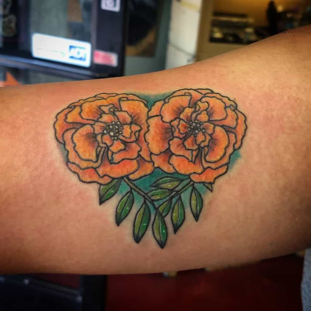 Vibrant tattoo featuring two bold orange marigolds with green leaves, accented by soft shading