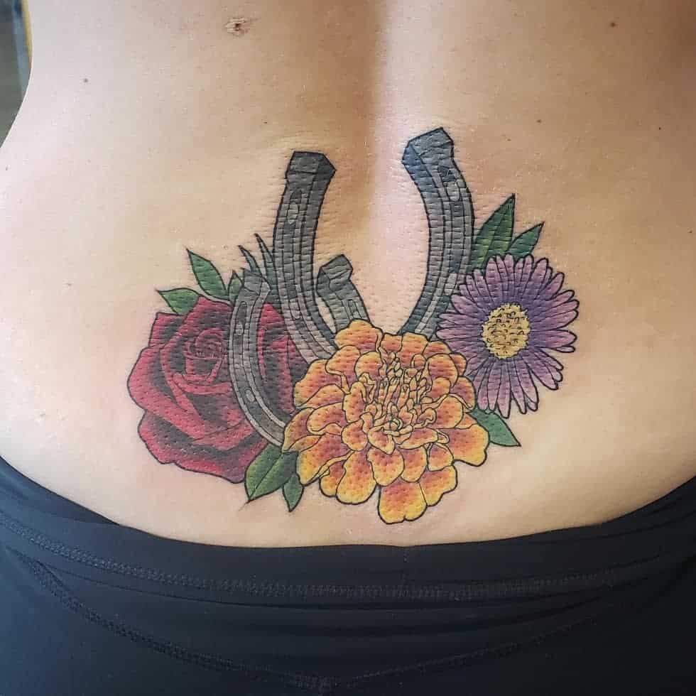 Colorful tattoo featuring a lucky horseshoe, vibrant marigold, red rose, and purple daisy, symbolizing luck and beauty