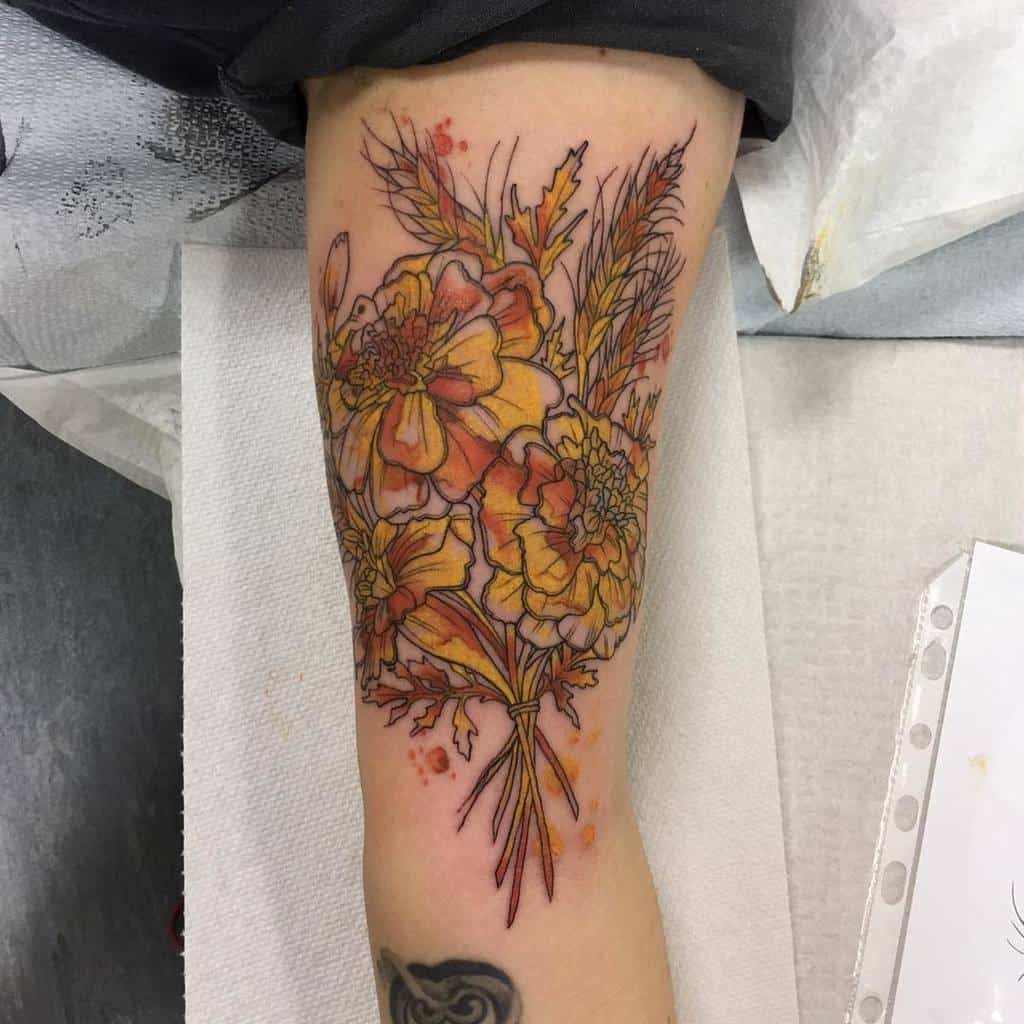 Intricate tattoo featuring a bouquet of orange marigolds and wheat, designed with fine linework, soft shading, and watercolor splashes