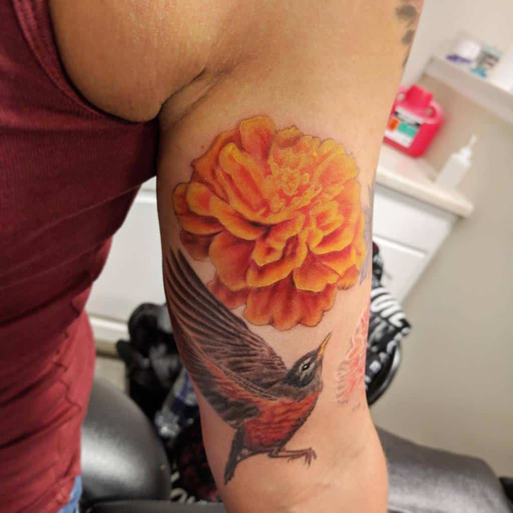 Vibrant tattoo featuring a bold orange marigold and a realistic flying bird, with rich shading and lifelike details