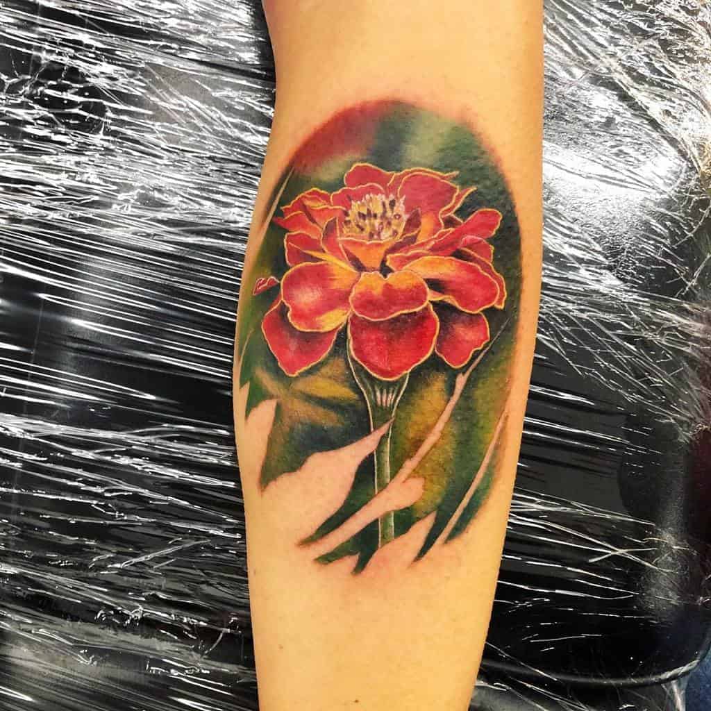 Colorful marigold tattoo on arm with green leaves