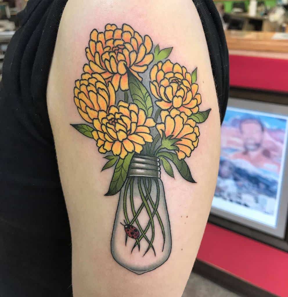 Creative tattoo featuring a bouquet of vibrant orange marigolds growing from a lightbulb, with a tiny ladybug on the glass