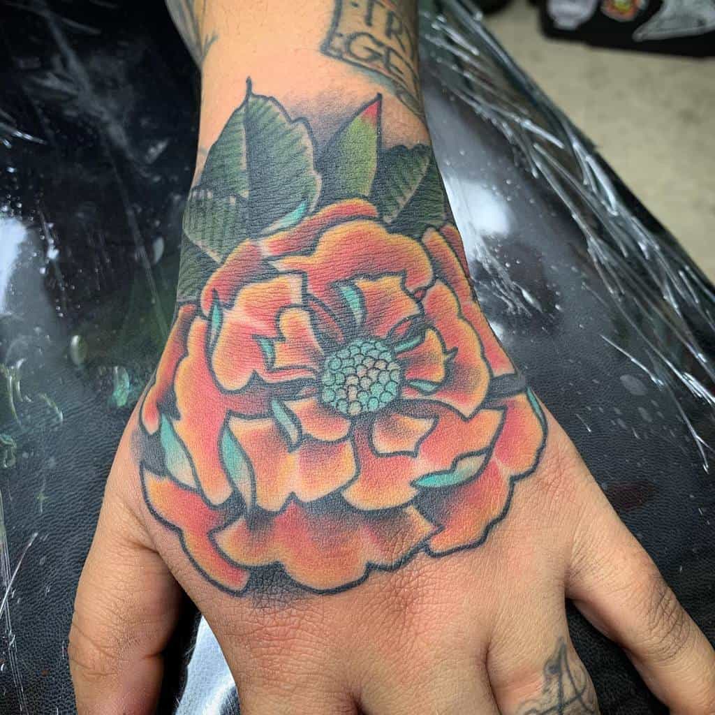 Bold tattoo featuring a vibrant orange marigold with intricate shading, deep green leaves, and a detailed teal center for contrast