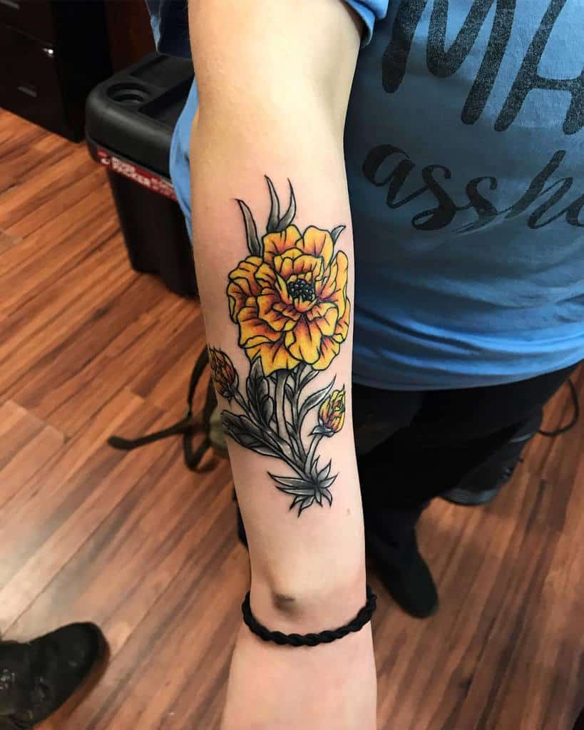 Bold tattoo featuring vibrant orange marigolds with fine black outlines, detailed shading, and flowing green leaves