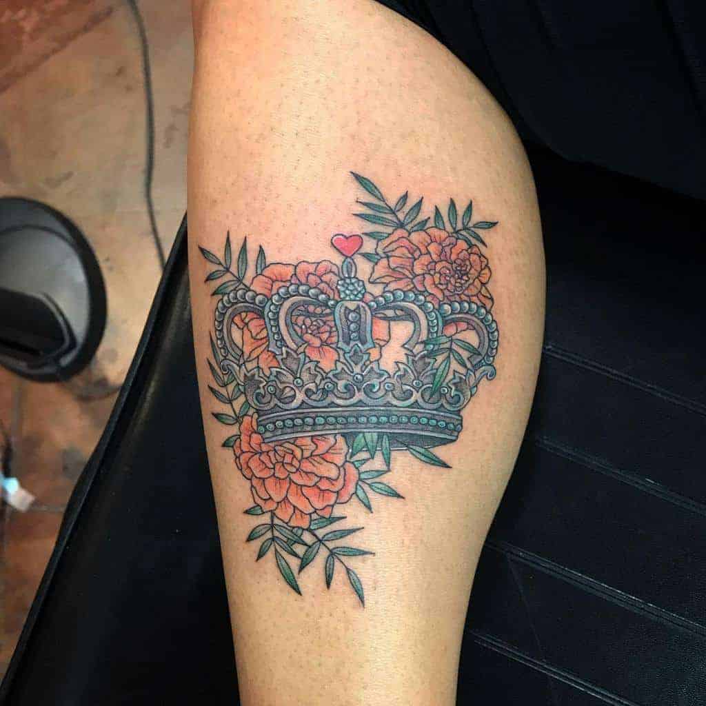 A colorful crown tattoo adorned with marigolds and leaves, blending elegance with vibrant floral details and a playful heart