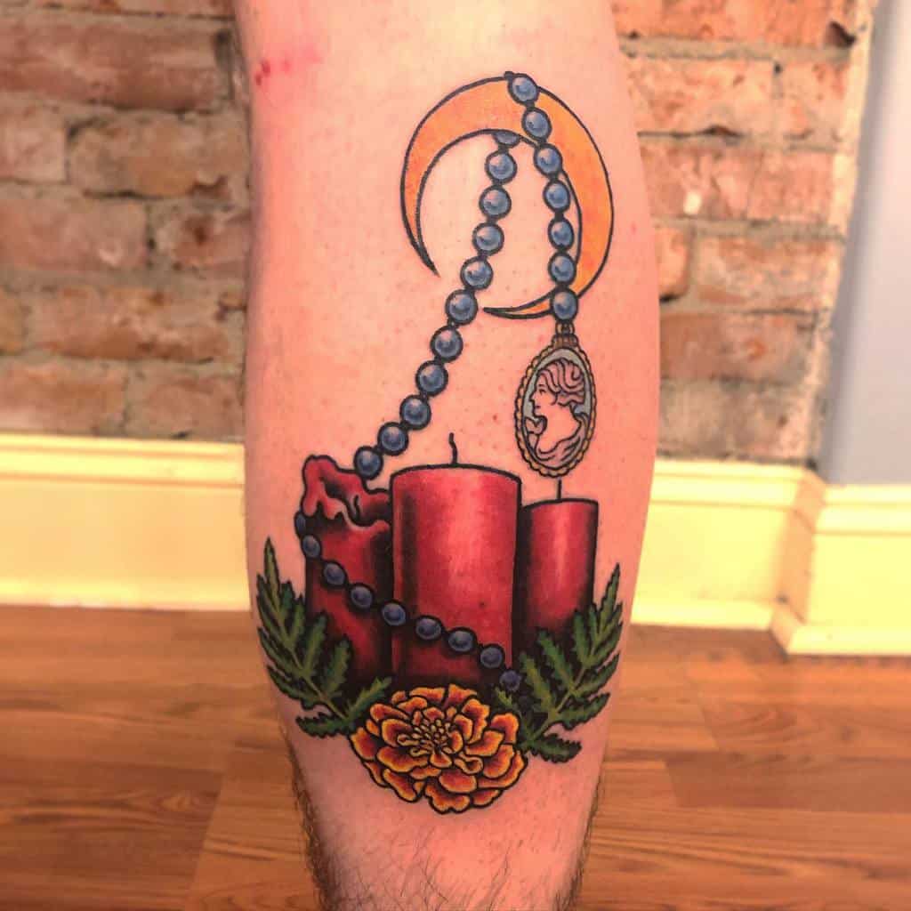 Colorful tattoo of three red candles, a marigold flower, greenery, and a rosary with a cameo with crescent moon