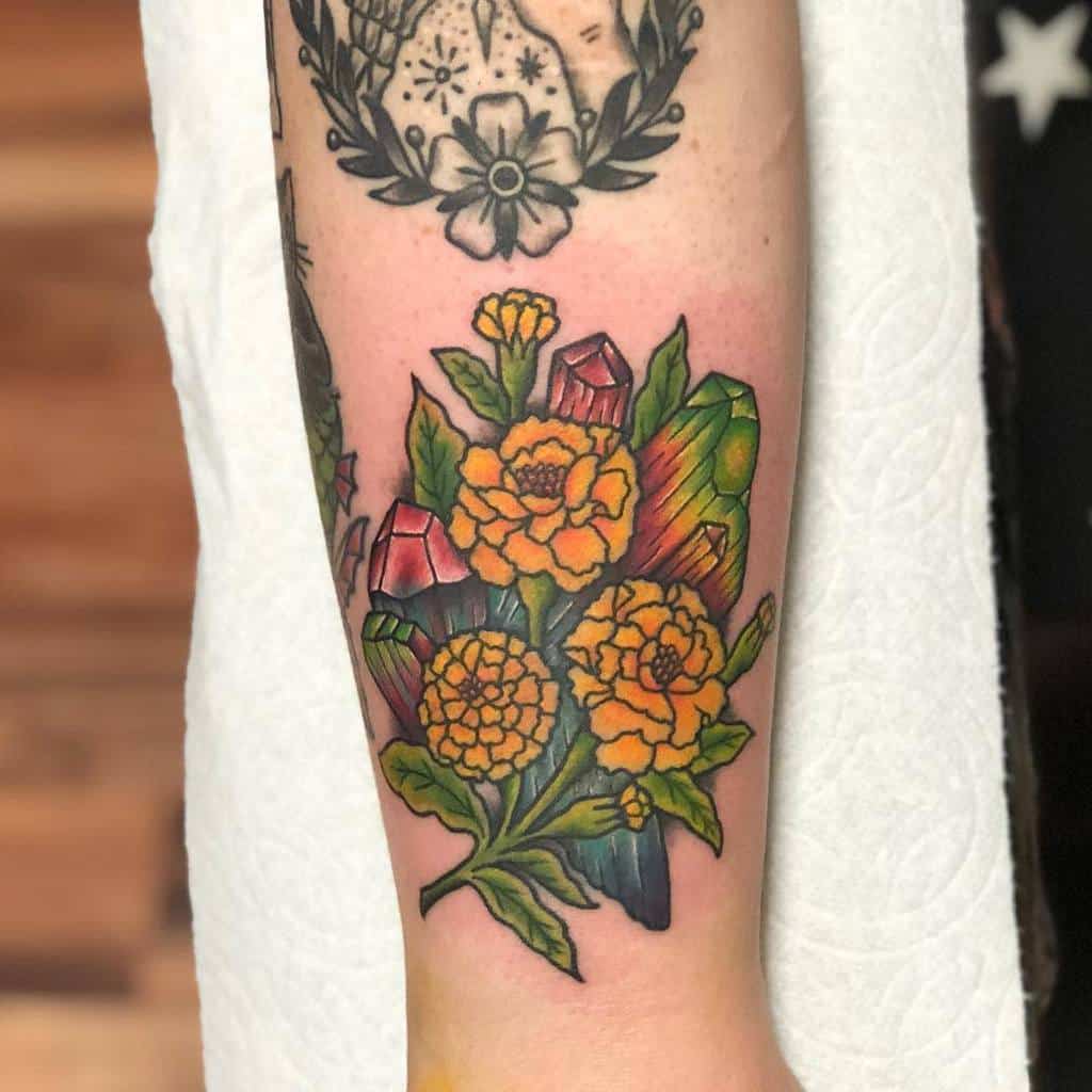 A colorful tattoo featuring yellow marigolds with green leaves and vibrant crystals