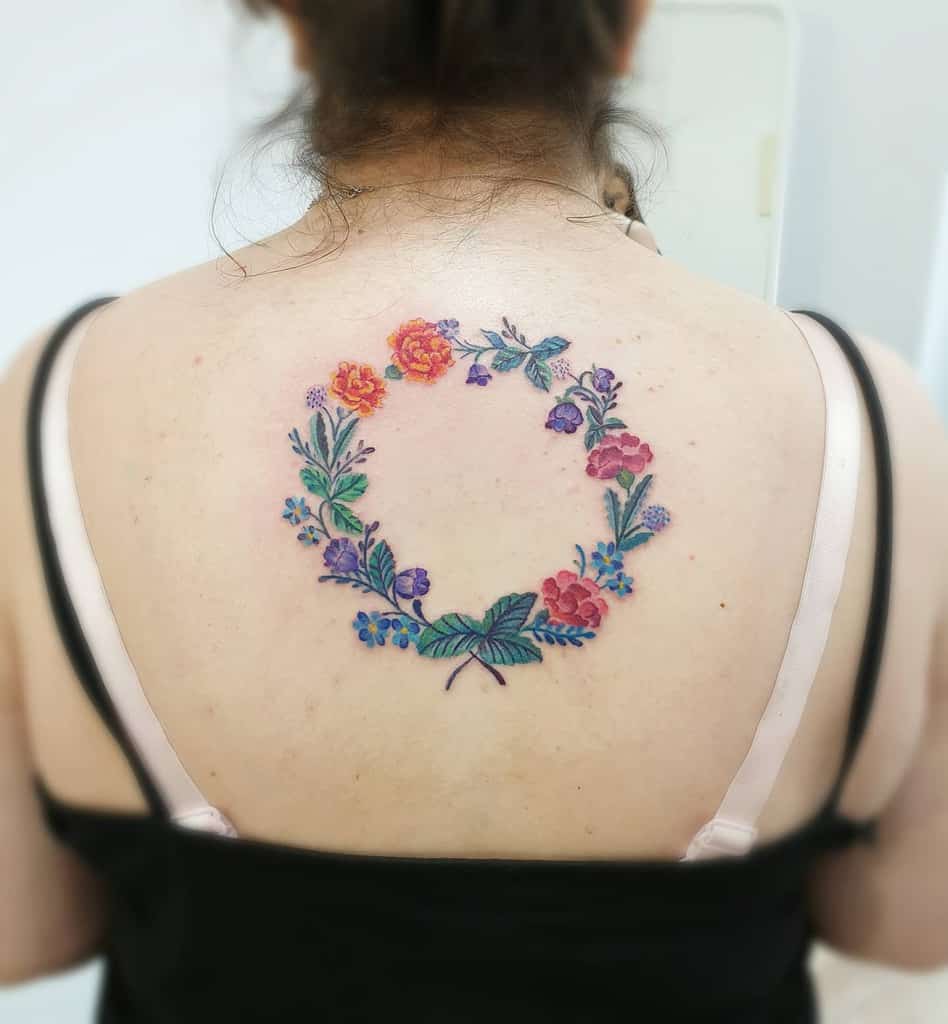 Delicate floral wreath tattoo, featuring colorful marigolds, violets, and greenery in a soft, watercolor-inspired design