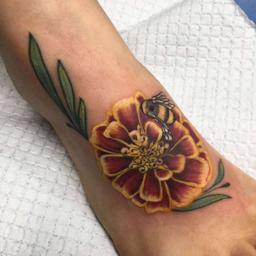 Realistic tattoo featuring a rich orange and red marigold with a detailed bumblebee resting on the petals, surrounded by green leaves
