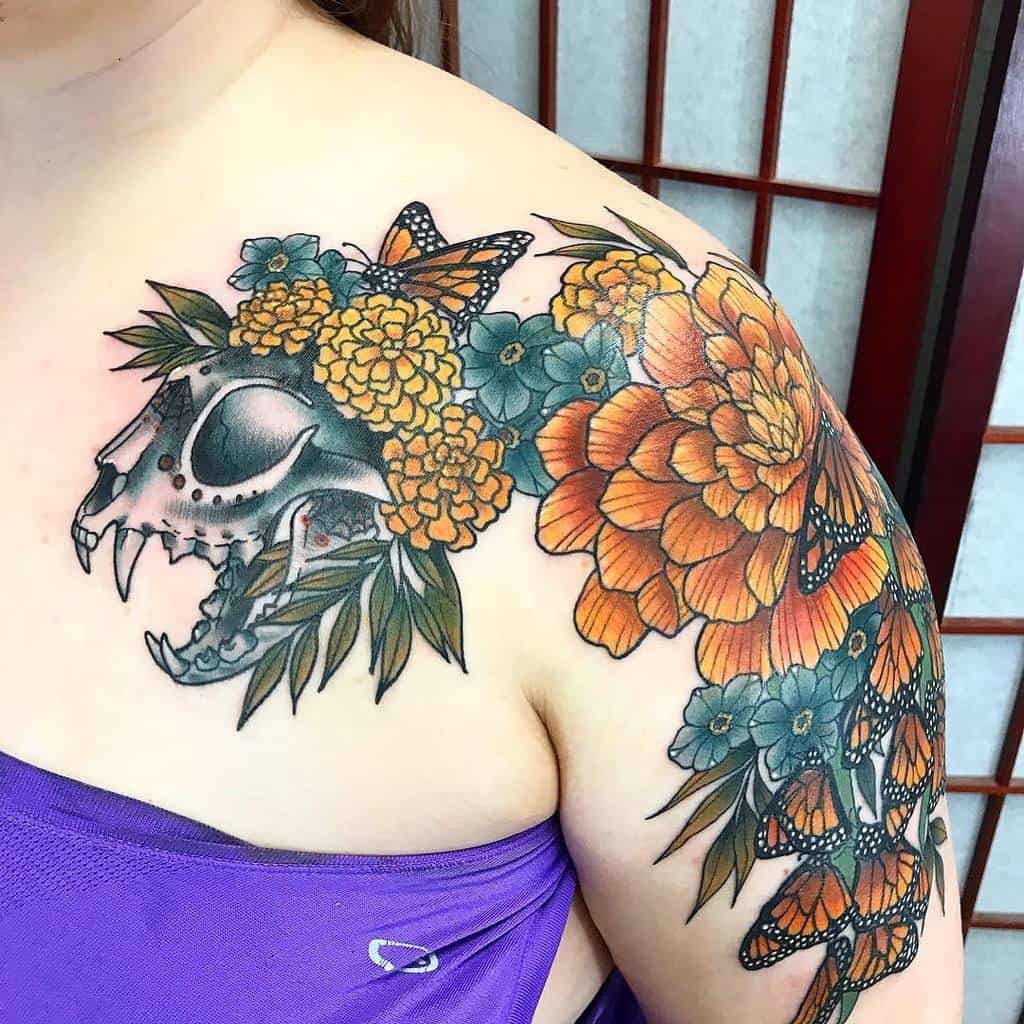 Vibrant tattoo featuring a detailed animal skull, bright marigold flowers, lush greenery, and monarch butterflies