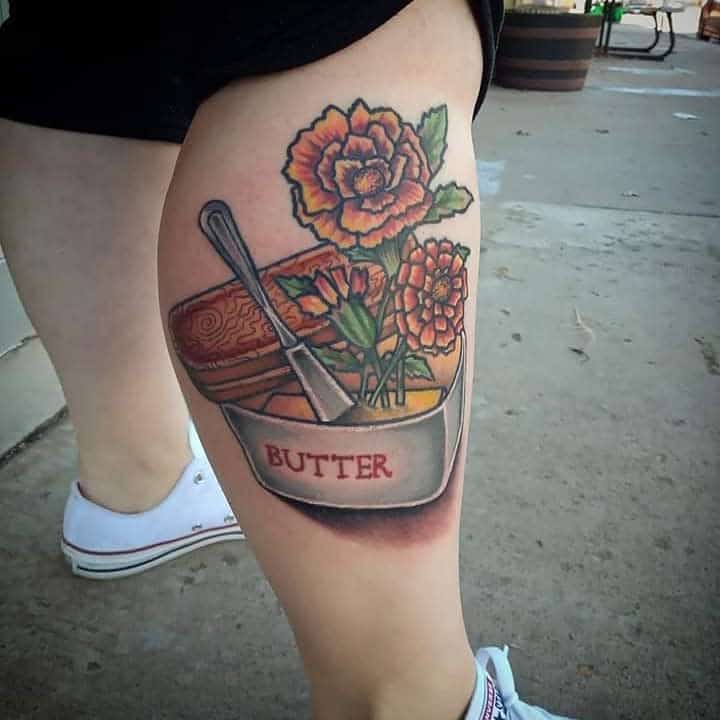 Tattoo of a butter dish with butter, marigold, bread and a knife, the dish is labeled "BUTTER"