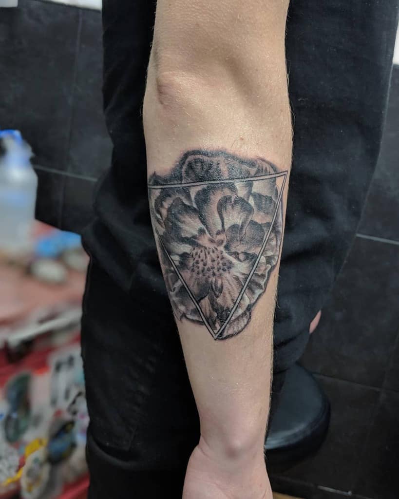 Black and grey tattoo featuring a realistic marigold partially enclosed within a geometric triangle
