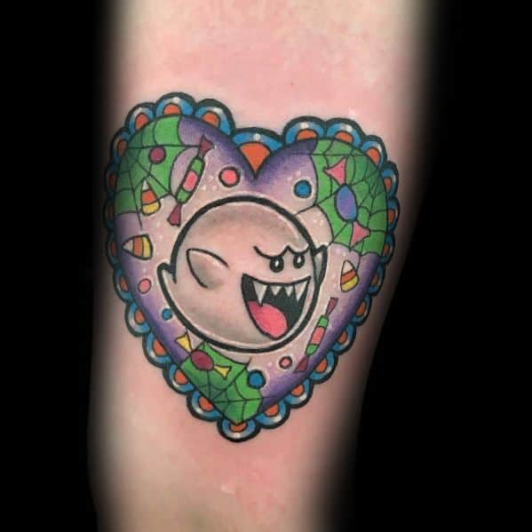 Mario ghost tattoo featuring Boo inside a colorful heart-shaped frame with candy and Halloween-inspired details, inked in vibrant shades.