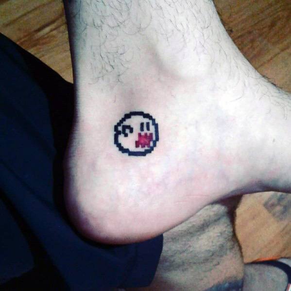 Pixelated Mario ghost tattoo featuring an 8-bit Boo with a playful grin and red tongue, inked in a small design on the ankle.