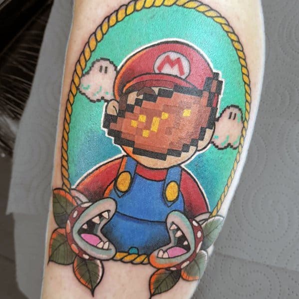 Unique *Super Mario* tattoo featuring a pixelated glitch effect on Mario’s face, framed by a rope border with Piranha Plants and cloud details.