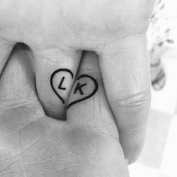 Matching finger tattoos forming a heart with the initials “L” and “K” on each half, symbolizing two halves of one love.