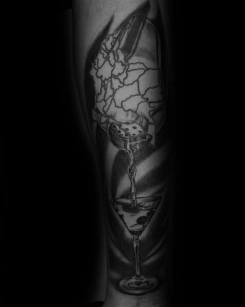 Black and grey martini glass tattoo featuring a cracked skull pouring liquid. A dramatic and surreal design with bold shading and intricate details.