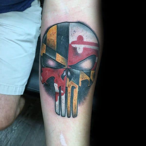 Punisher-style skull tattoo filled with the Maryland flag pattern on the forearm, blending bold colors with an edgy and fierce design.