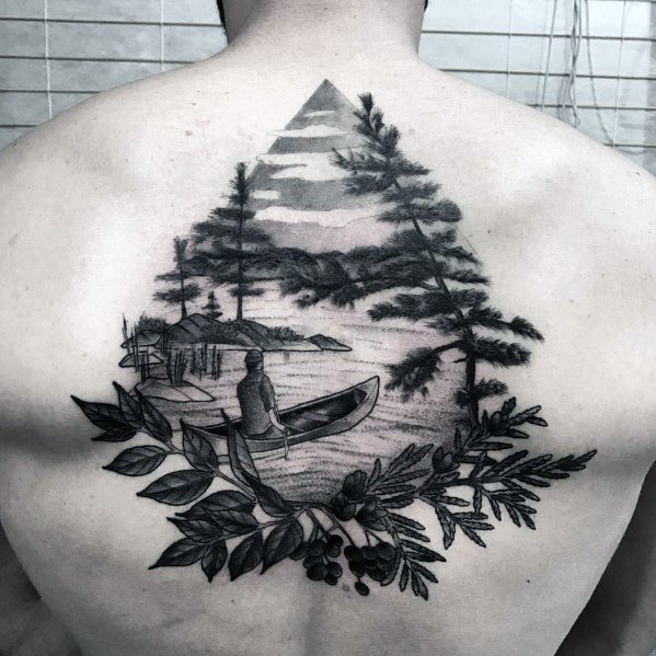 Alt text: Detailed black and grey tattoo of a person in a canoe on a peaceful lake, surrounded by trees and a mountain, framed by lush foliage.