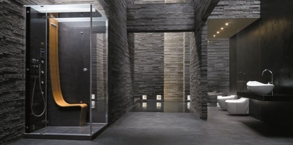 Modern, minimalist bathroom with a glass shower, sinks, and toilets against dark walls