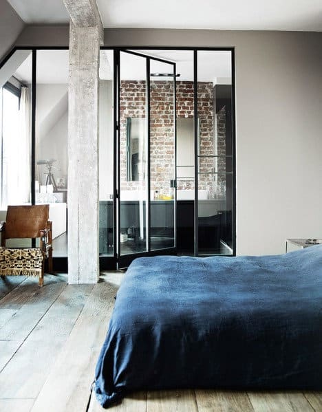 Modern bedroom with a navy bedspread and a glass partition revealing a bathroom