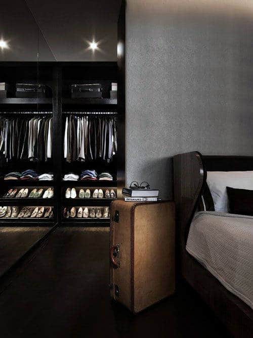Dark men’s bedroom with walk-in closet and organized shoe and clothing shelves.