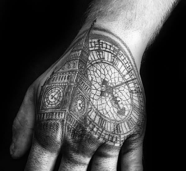 Detailed black and grey tattoo of Big Ben with its clock face on the hand, showcasing intricate details and shading that capture the clock's structure and design.