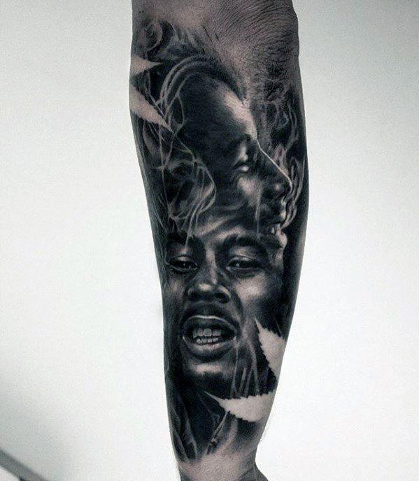 Dual-portrait Bob Marley tattoo with one calm and one smiling expression, surrounded by smoke and leaves in a detailed black and gray design.