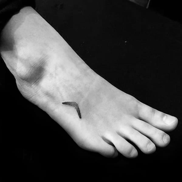 Tiny minimalist boomerang tattoo on the top of the foot, created with fine dotwork for a subtle and sleek look.