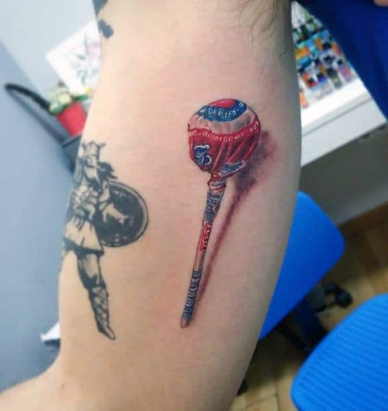 Realistic Chupa Chups lollipop tattoo with detailed shading and highlights, creating a striking 3D effect on the arm.