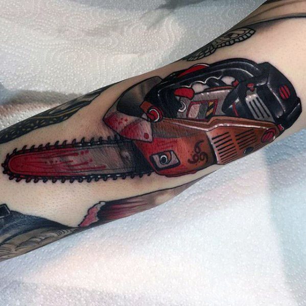Detailed red and black chainsaw tattoo with realistic shading and blood-stained blade, stretching along the forearm in a bold style.