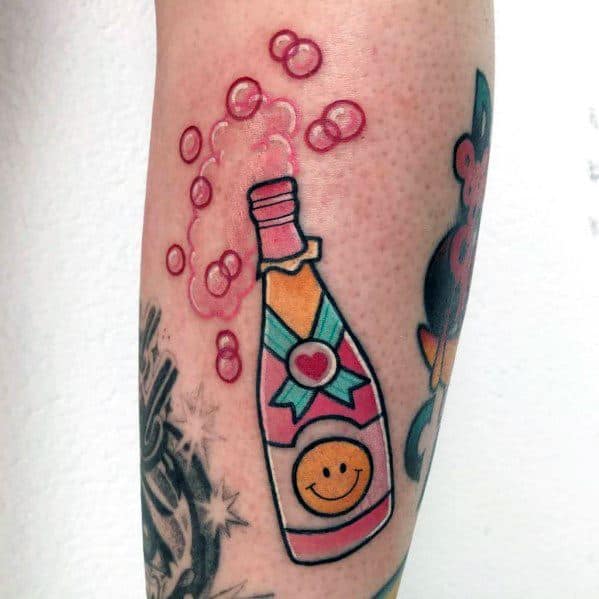 Tattoo of a colorful champagne bottle with a smiley face label, popping open with bubbles rising.