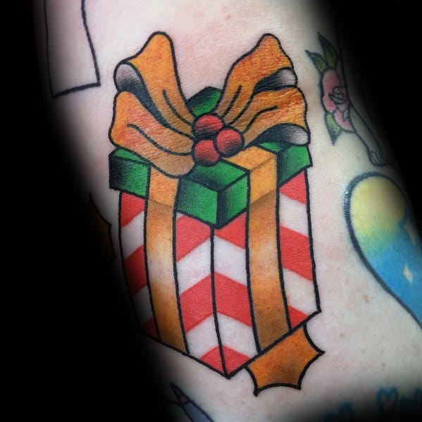 Christmas tattoo of a festive gift box with red and white stripes, wrapped in a green ribbon and topped with a gold bow and holly berries for a classic holiday look.